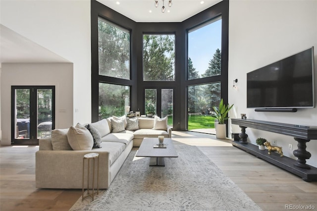 living room featuring french doors, light hardwood / wood-style flooring, a towering ceiling, and a notable chandelier