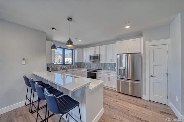 kitchen featuring a breakfast bar area, a peninsula, a sink, white cabinetry, and appliances with stainless steel finishes