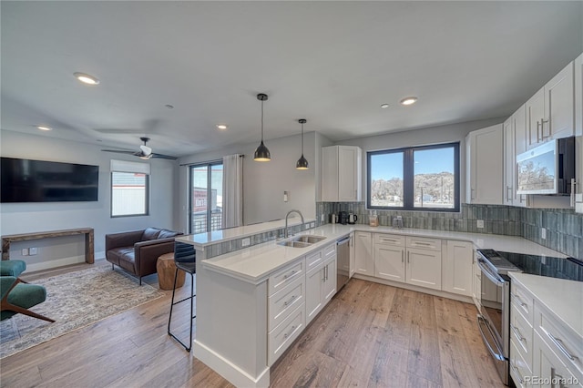 kitchen featuring appliances with stainless steel finishes, a sink, a peninsula, and light wood-style flooring