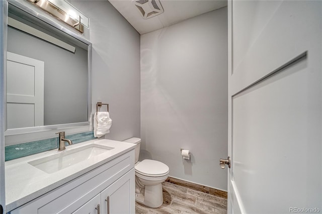 half bathroom with visible vents, toilet, vanity, wood finished floors, and baseboards