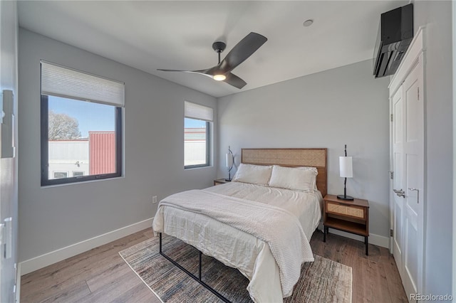 bedroom with ceiling fan, light wood-type flooring, a wall mounted air conditioner, and baseboards