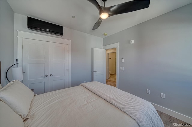 bedroom featuring baseboards, a ceiling fan, wood finished floors, a wall mounted air conditioner, and a closet