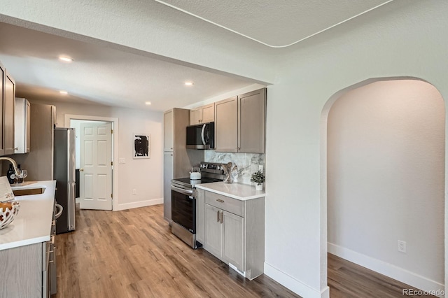 5555 Julian St, Denver, CO 80221 - kitchen featuring appliances with stainless steel finishes, arched walkways, a sink, light wood-style flooring, and baseboards