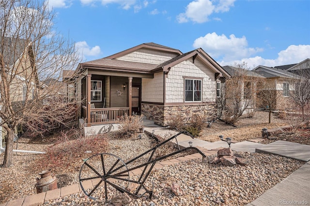 view of front of property featuring covered porch, stone siding, and roof with shingles