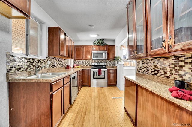 7819 Tejon St, Denver, CO 80221 - kitchen with appliances with stainless steel finishes, backsplash, light wood-type flooring, a textured ceiling, and glass insert cabinets