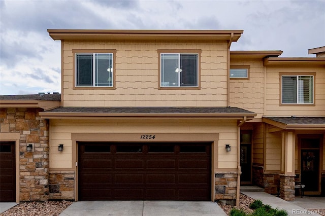 multi unit property with stone siding, an attached garage, concrete driveway, and a shingled roof