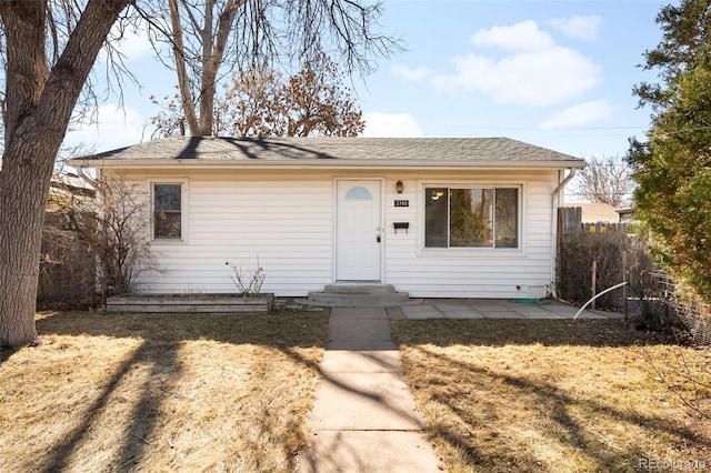 view of front facade with entry steps, a patio, a shingled roof, and a front yard