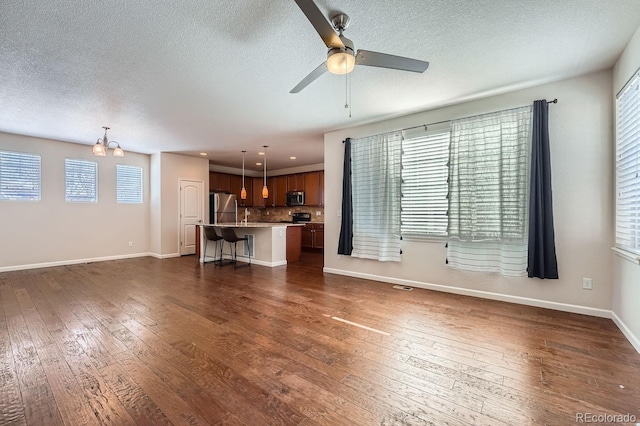 unfurnished living room with a textured ceiling, dark wood-type flooring, and ceiling fan with notable chandelier