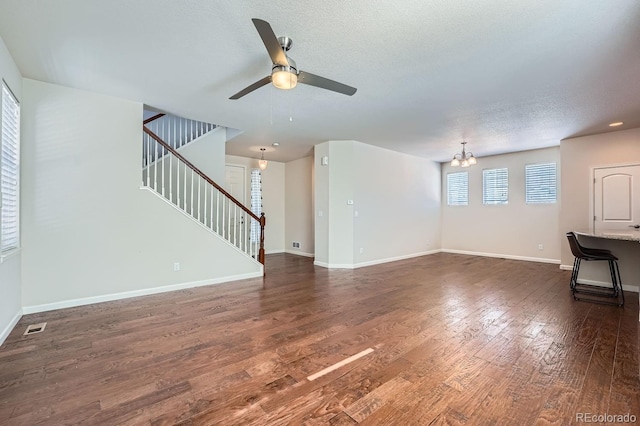 unfurnished living room with a textured ceiling, dark wood-type flooring, and ceiling fan with notable chandelier