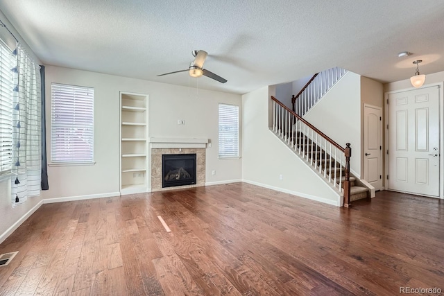 unfurnished living room with a textured ceiling, a wealth of natural light, a fireplace, built in features, and ceiling fan