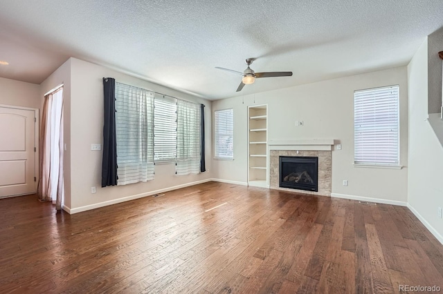 unfurnished living room featuring a tiled fireplace, ceiling fan, dark hardwood / wood-style floors, a textured ceiling, and built in features