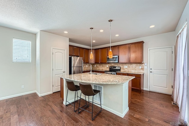 kitchen featuring hanging light fixtures, a center island with sink, backsplash, appliances with stainless steel finishes, and sink