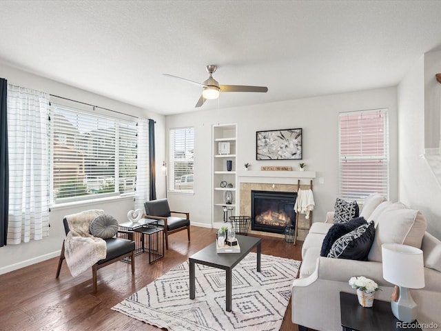 living room featuring baseboards, a ceiling fan, a glass covered fireplace, and wood finished floors