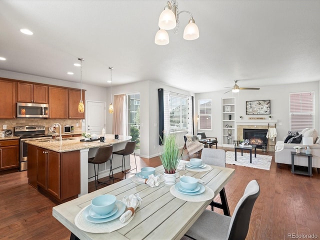 dining room featuring ceiling fan with notable chandelier, a fireplace, baseboards, dark wood-style floors, and recessed lighting