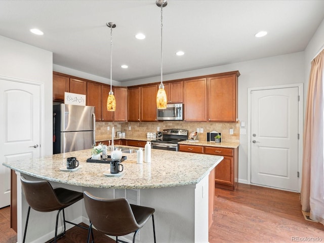 kitchen featuring stainless steel appliances, decorative backsplash, light stone countertops, brown cabinetry, and a breakfast bar