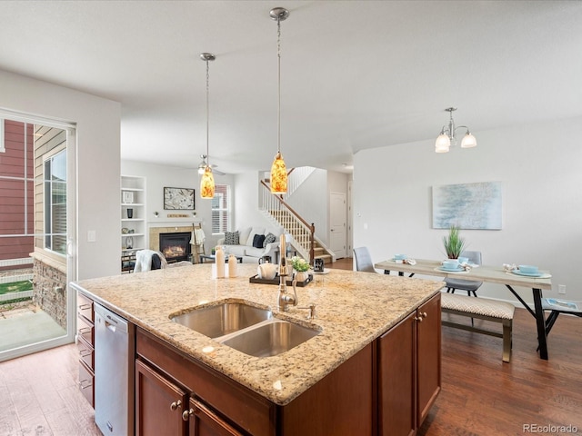 kitchen with a sink, dishwasher, a fireplace, dark wood-type flooring, and hanging light fixtures