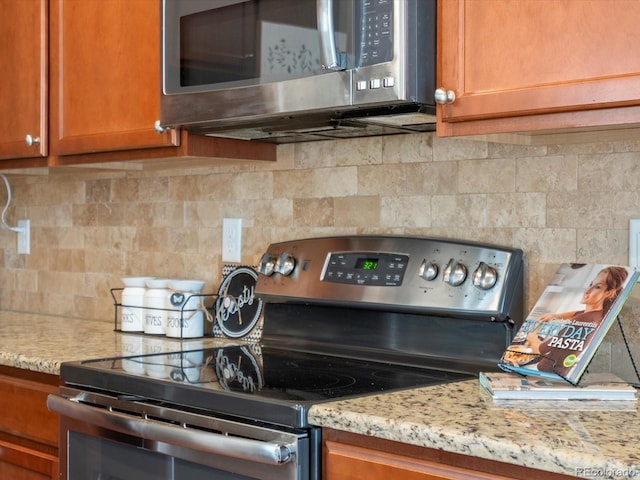 kitchen with decorative backsplash, brown cabinets, appliances with stainless steel finishes, and light stone countertops