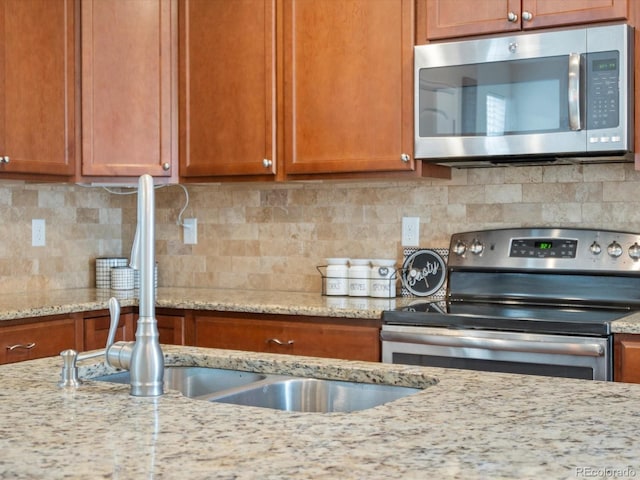 kitchen featuring backsplash, light stone counters, brown cabinets, and appliances with stainless steel finishes