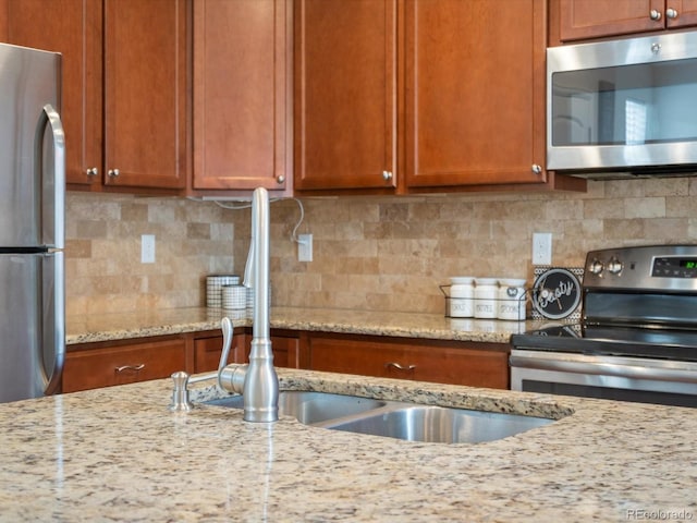 kitchen with stainless steel appliances, decorative backsplash, brown cabinets, and light stone counters