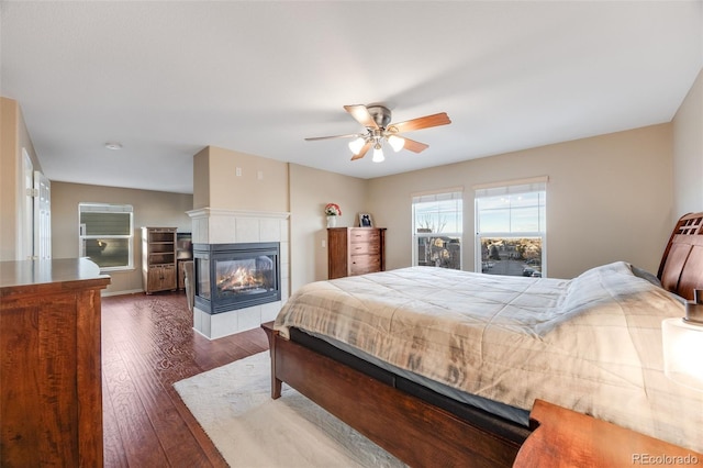 bedroom with dark wood-style flooring, a ceiling fan, and a fireplace
