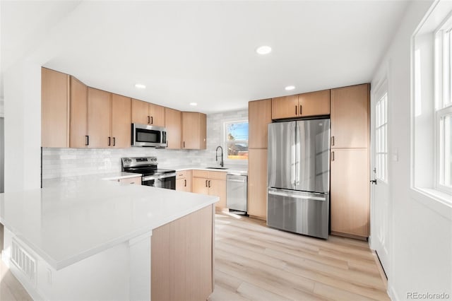 kitchen featuring sink, kitchen peninsula, decorative backsplash, light brown cabinetry, and appliances with stainless steel finishes