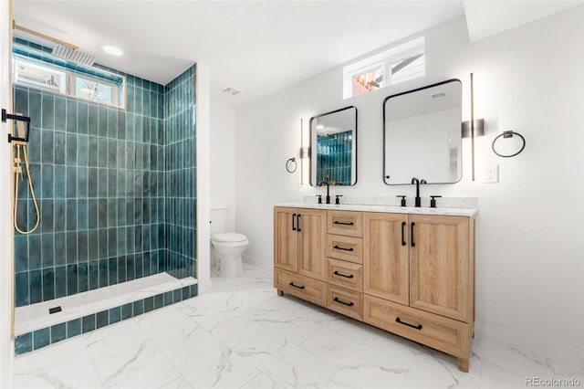 bathroom with a tile shower, vanity, toilet, and a wealth of natural light