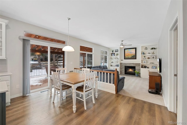 dining space with ceiling fan, a fireplace, built in features, and wood-type flooring