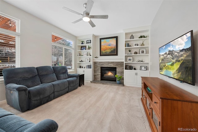 carpeted living room with ceiling fan, a stone fireplace, and built in features