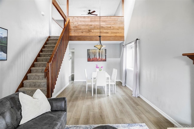 dining room featuring ceiling fan, light wood-type flooring, and a towering ceiling