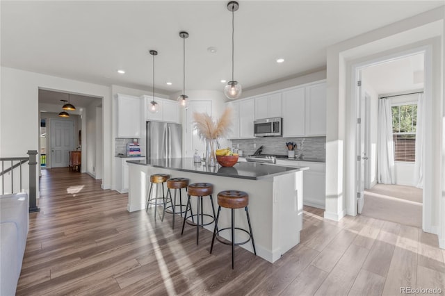 14431 Forest St, Thornton, CO 80602 - kitchen with stainless steel appliances, light wood finished floors, a breakfast bar, decorative backsplash, and white cabinets