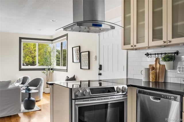 kitchen featuring island range hood, stainless steel appliances, tasteful backsplash, dark countertops, and light wood-style floors