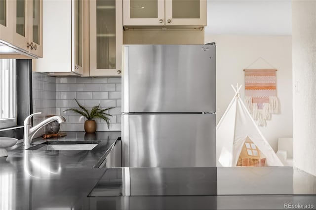 kitchen with freestanding refrigerator, a sink, backsplash, and glass insert cabinets