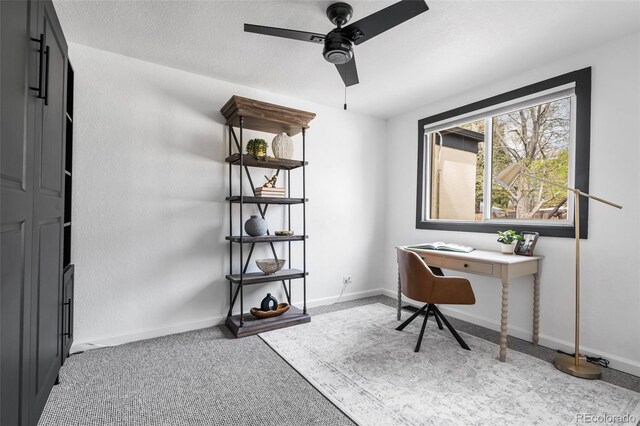 carpeted office space featuring a ceiling fan and baseboards