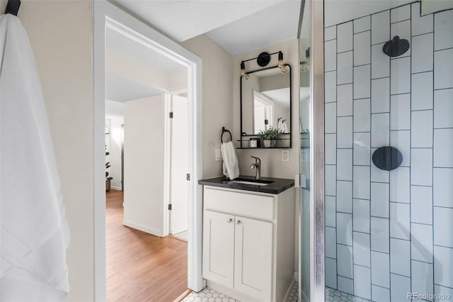 full bathroom with tiled shower, vanity, and wood finished floors