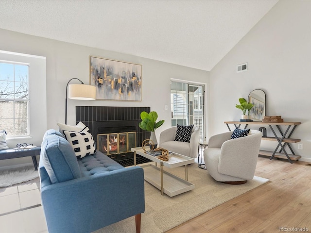 living area with lofted ceiling, visible vents, a glass covered fireplace, wood finished floors, and baseboards