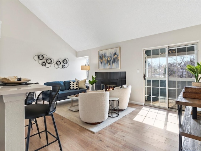 living area featuring high vaulted ceiling, wood finished floors, a glass covered fireplace, and baseboards