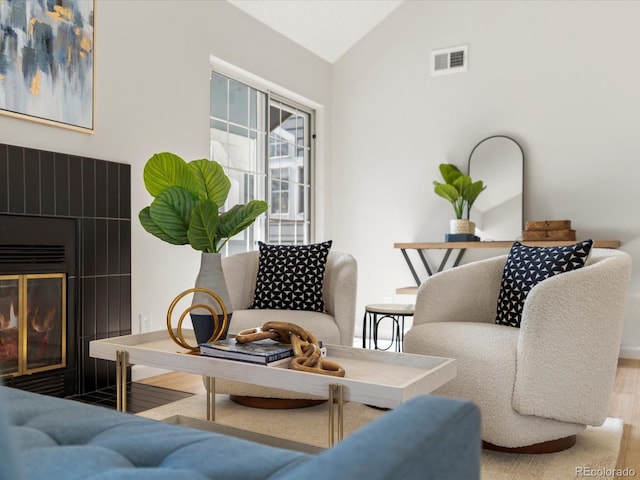 living room featuring lofted ceiling, visible vents, a glass covered fireplace, and wood finished floors