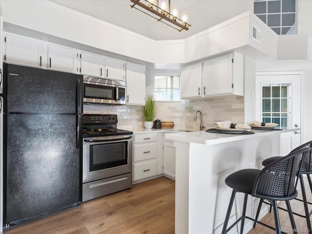 kitchen featuring a sink, white cabinetry, light countertops, appliances with stainless steel finishes, and a kitchen bar