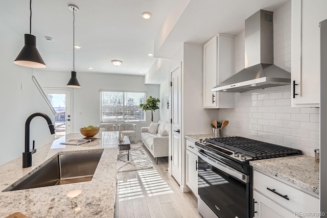 15345 W 69th Dr, Arvada, CO 80007 - kitchen with wall chimney range hood, gas range, a sink, open floor plan, and light wood finished floors