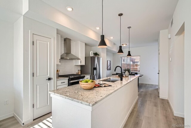 15345 W 69th Dr, Arvada, CO 80007 - kitchen with wall chimney range hood, stainless steel appliances, a sink, white cabinets, and light wood finished floors