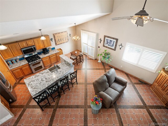 kitchen with sink, a breakfast bar area, appliances with stainless steel finishes, hanging light fixtures, and light stone counters