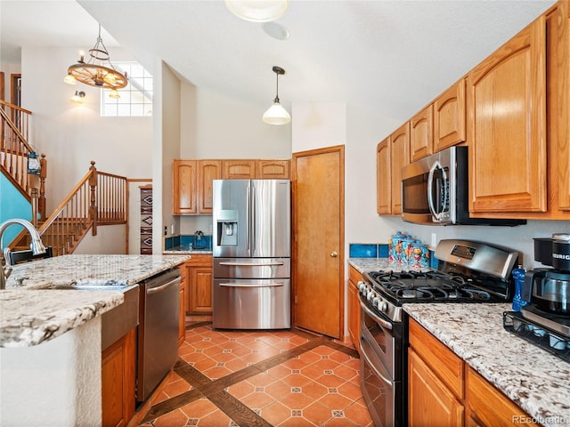 kitchen with hanging light fixtures, light stone countertops, sink, and appliances with stainless steel finishes