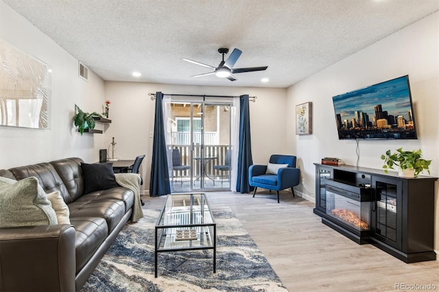 living room featuring visible vents, a glass covered fireplace, a textured ceiling, light wood-type flooring, and baseboards