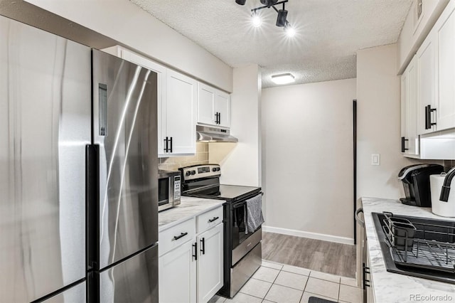 kitchen with a textured ceiling, under cabinet range hood, white cabinets, appliances with stainless steel finishes, and tasteful backsplash