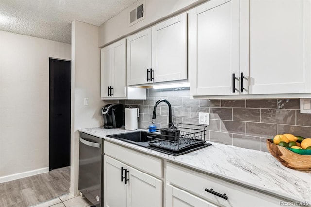 kitchen featuring light stone counters, tasteful backsplash, visible vents, stainless steel dishwasher, and a sink