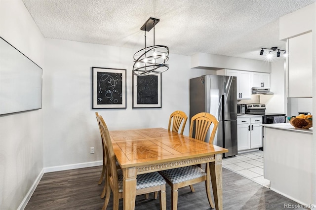 dining room with light wood-type flooring, a notable chandelier, a textured ceiling, and baseboards