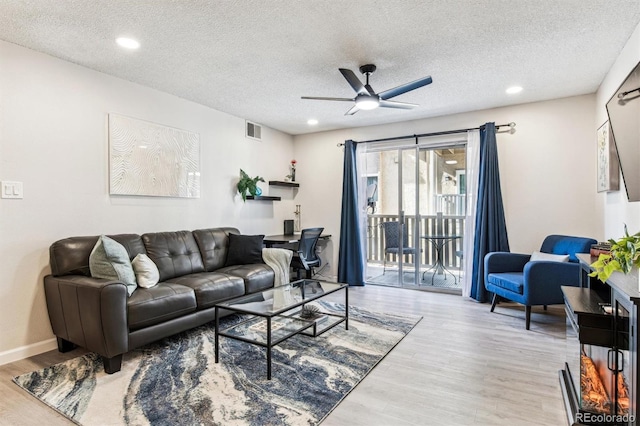 living area featuring a ceiling fan, a textured ceiling, visible vents, and wood finished floors