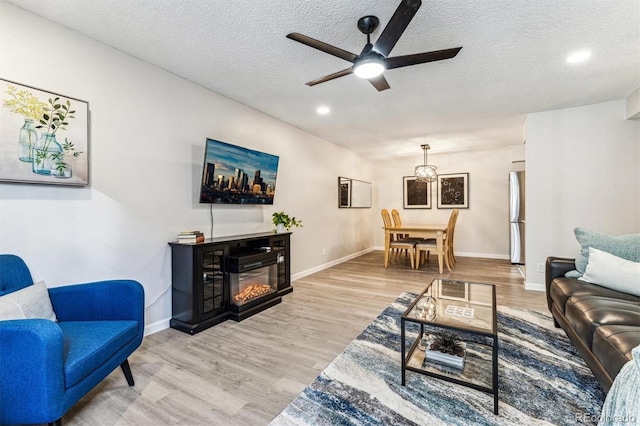 living area featuring a textured ceiling, light wood finished floors, a glass covered fireplace, and baseboards