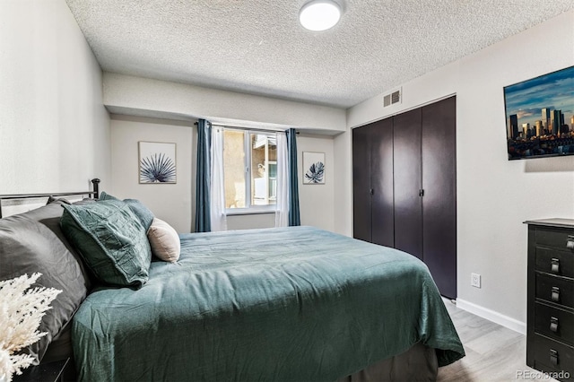 bedroom with baseboards, visible vents, wood finished floors, a textured ceiling, and a closet