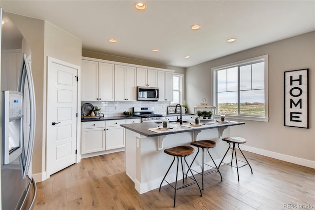 kitchen with decorative backsplash, dark countertops, a breakfast bar area, stainless steel appliances, and a sink